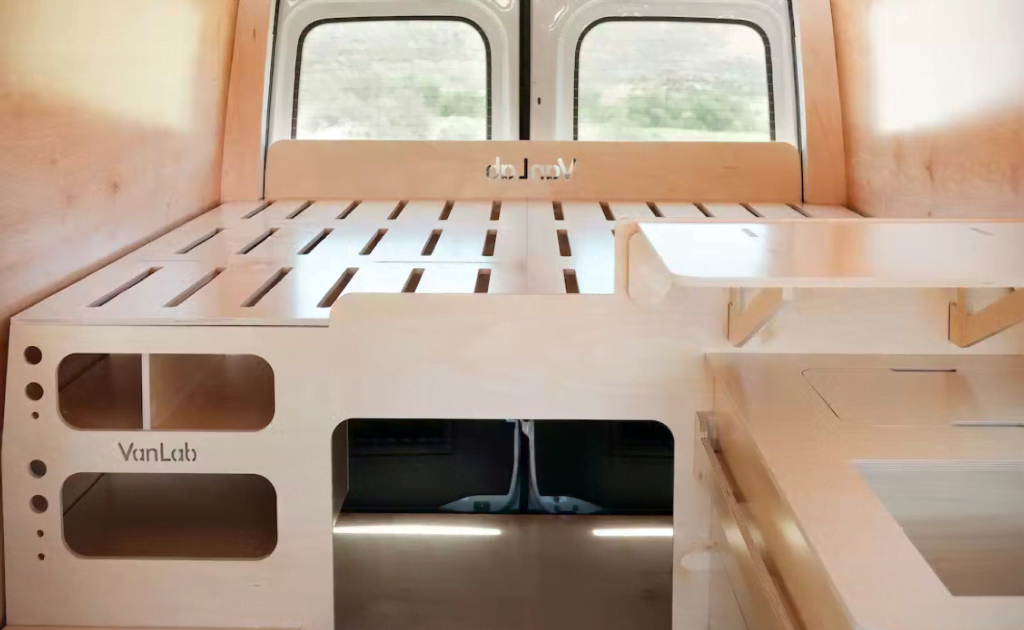 Modular wooden bed platform installed inside a camper van, featuring storage compartments and a modern minimalist design.