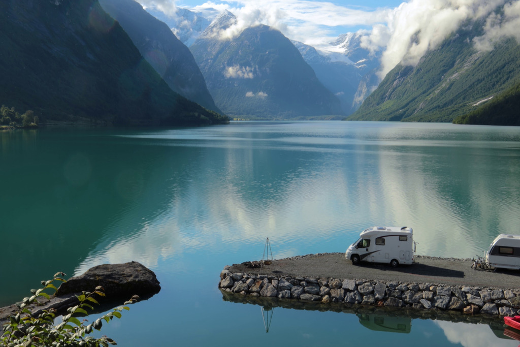 RV parked by a serene lake surrounded by mountains, showcasing the beauty of off-grid camping and sustainable RV living