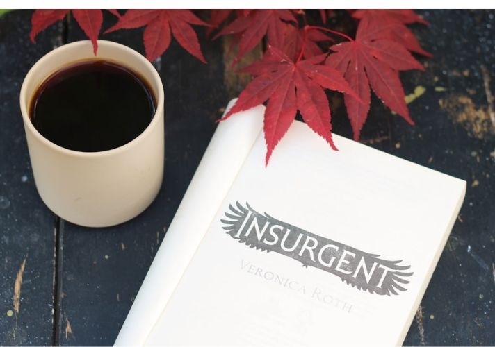 Cup of black coffee next to a book and red autumn leaves on a dark wooden table