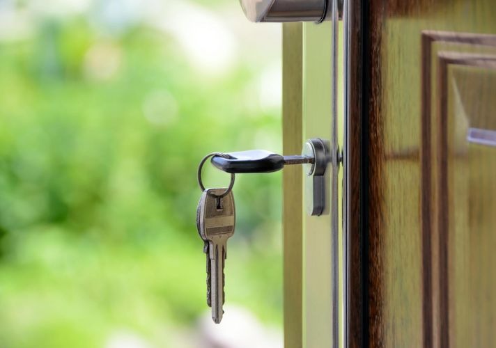 Close-up of house keys hanging in a front door lock with a green garden blurred in the background