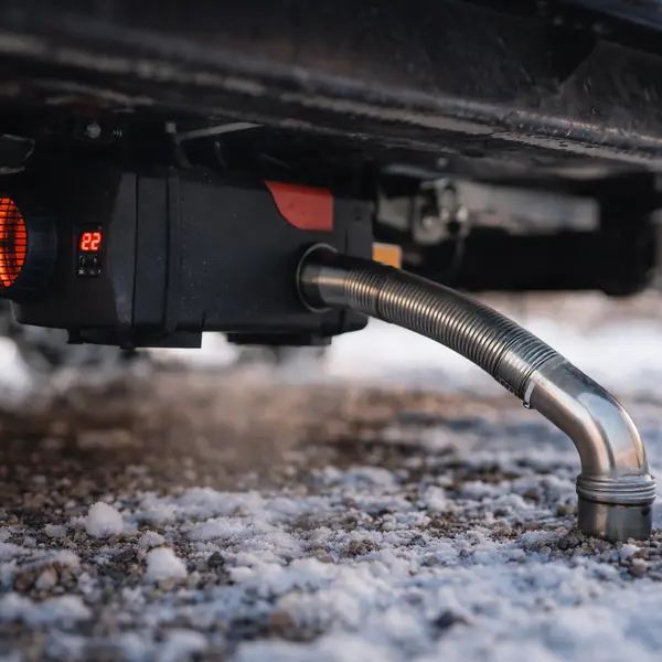 chinese diesel heater mounted under rv chassis with stainless steel exhaust pipe and glowing temperature gauge in snow on ground during winter boondocking setup