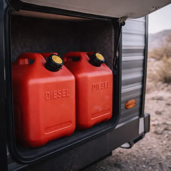 two 5-gallon red diesel jerry cans stored in rv exterior compartment with desert landscape visible through open compartment door in winter daylight
