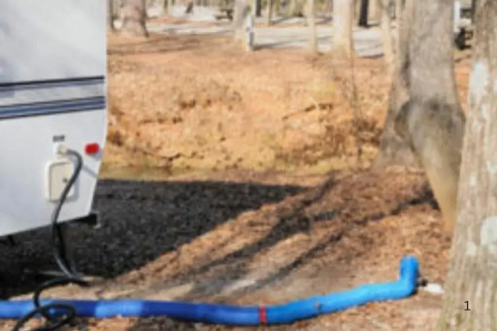 RV sewer hose connected to a camper for wastewater drainage at a campsite with trees outdoors